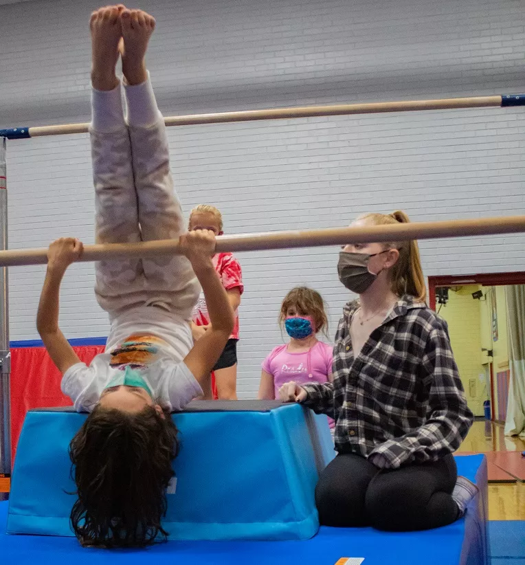 Child learning to flip on a gymnastics' bar