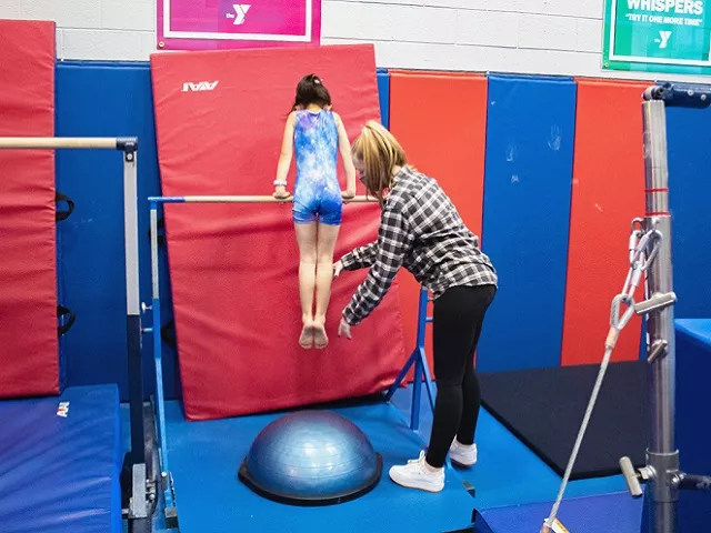 Child on a gymnastics' bar being coached