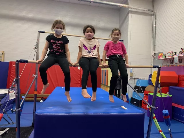 Three children smiling on a gymnastics bar